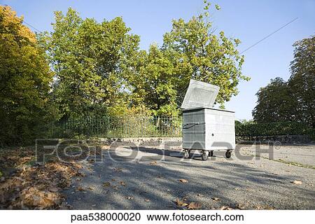 Stock Image - Small dumpster in parking lot at edge of wooded area. Fotosearch