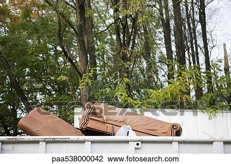 Stock Image - Sofa sticking out of top of dumpster. Fotosearch