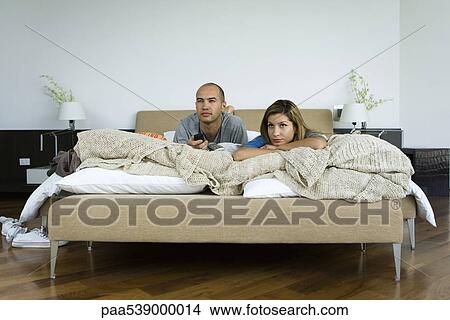 Picture - Couple lying in bed watching television. Fotosearch
