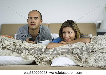 Couple lying on bed watching TV together View Large Photo Image Stock Photo - Couple lying on bed watching TV together. Fotosearch