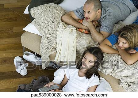 Family lying in bed watching television, directly above View Large Photo Image Stock Photo - Family lying in bed watching television, directly above. Fotosearch