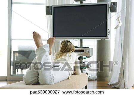 Stock Photo - Female lying on stomach watching flat screen TV, rear view. Fotosearch