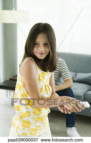Stock Photo - Girl playing video game with wireless controller, man sitting in background. Fotosearch