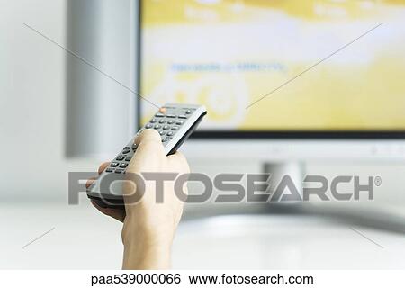Stock Photograph - Hand holding remote control, television in background. Fotosearch