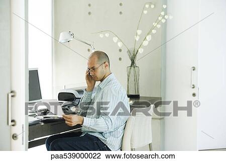 Man working in home office, using cell phone and looking at document View Large Photo Image Stock Image - Man working in home office, using cell phone and looking at document. Fotosearch