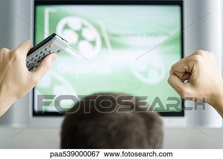 Stock Photo - Person watching flat screen television, hands raised in air, cropped view. Fotosearch
