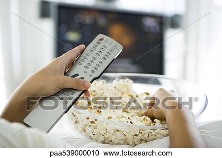 Person watching television, holding remote control and bowl of popcorn, cropped view View Large Photo Image Stock Image - Person watching television, holding remote control and bowl of popcorn, cropped view. Fotosearch