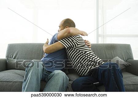 Stock Image - two men ambracing on sofa. Fotosearch