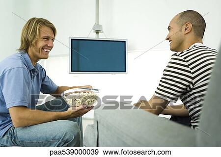 Two men chatting and eating popcorn, flat screen TV in background View Large Photo Image Stock Photo - Two men chatting and eating popcorn, flat screen TV in background. Fotosearch