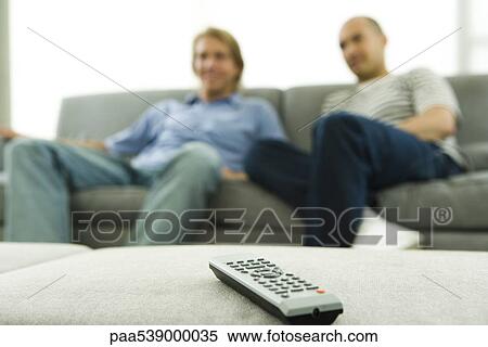 Stock Photography - Two men sitting on sofa, focus on remote control in foreground. Fotosearch