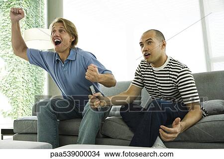 Picture - Two men watching TV and cheering on sofa. Fotosearch