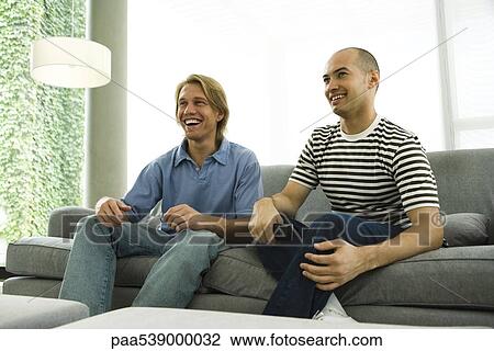 Stock Image - Two men watching TV on sofa. Fotosearch