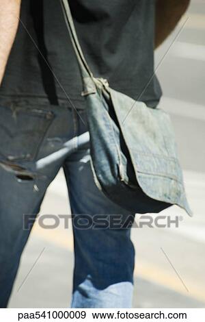 Stock Photo - Person carrying denim shoulder bag, rear view, cropped. Fotosearch