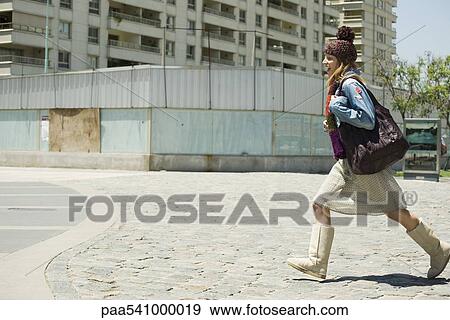 Trendy young woman walking on sidewalk, side view View Large Photo Image Stock Photo - Trendy young woman walking on sidewalk, side view. Fotosearch