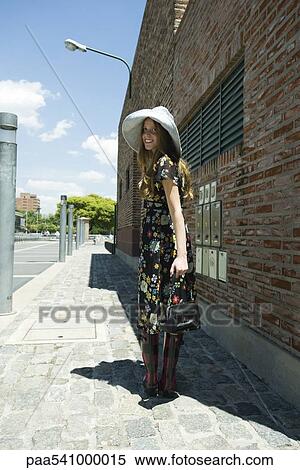 Trendy young woman walking on sidewalk, smiling over shoulder at camera View Large Photo Image Stock Photography - Trendy young woman walking on sidewalk, smiling over shoulder at camera. Fotosearch