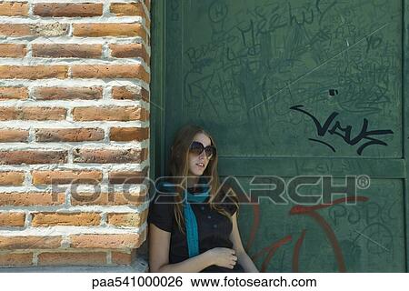Young woman in sunglasses leaning against wall View Large Photo Image Stock Photograph - Young woman in sunglasses leaning against wall. Fotosearch