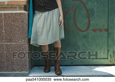 Stock Photography - Young woman in trendy clothing leaning against wall, low section. Fotosearch