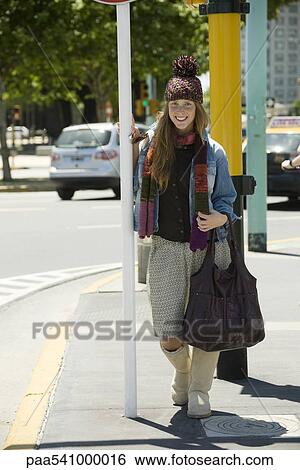 Stock Photograph - Young woman in trendy clothing standing on sidewalk, full length portrait. Fotosearch