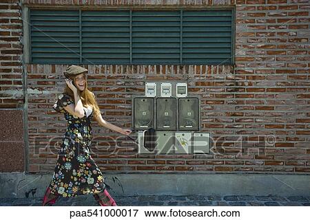 Stock Photo - Young woman in trendy clothing walking on sidewalk, chatting on cell phone. Fotosearch