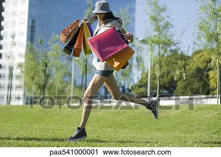 Young woman running through park, carrying several shopping bags View Large Photo Image Stock Image - Young woman running through park, carrying several shopping bags. Fotosearch