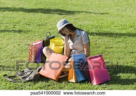 Young woman sitting in park, surrounded by shopping bags View Large Photo Image Stock Image - Young woman sitting in park, surrounded by shopping bags. Fotosearch