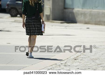 Young woman walking along sidewalk, carrying book, rear view View Large Photo Image Stock Image - Young woman walking along sidewalk, carrying book, rear view. Fotosearch