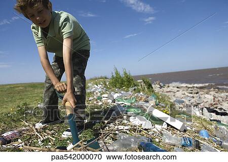 Stock Image - Boy cleaning up polluted shore with shovel, low angle view. Fotosearch