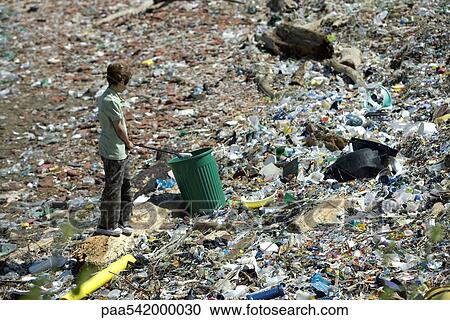 Stock Image - Boy picking up garbage in dump, high angle view. Fotosearch