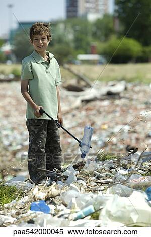 Stock Photography - Boy picking up plastic bottle in dump, smiling at camera. Fotosearch