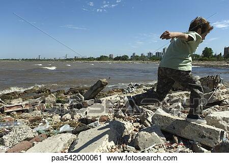 Boy running on shore littered with debris, city in background View Large Photo Image Stock Image - Boy running on shore littered with debris, city in background. Fotosearch