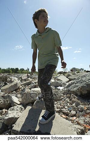 Picture - Boy standing on heap of rubble, backlit. Fotosearch