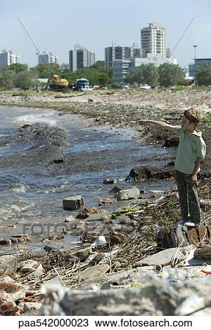 Boy standing on polluted shore, looking at view, pointing View Large Photo Image Stock Image - Boy standing on polluted shore, looking at view, pointing. Fotosearch