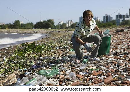 Stock Image - Male picking up trash on polluted shore. Fotosearch