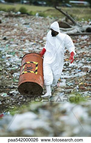 Stock Photograph - Person in protective suit carrying barrel of hazardous waste. Fotosearch