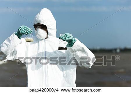 Person in protective suit holding flasks filled with polluted water View Large Photo Image Picture - Person in protective suit holding flasks filled with polluted water. Fotosearch