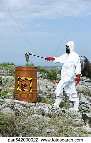 Stock Image - Person in protective suit placing dead fish in hazardous waste barrel. Fotosearch