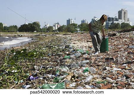 Person picking up trash on polluted shore, city in background View Large Photo Image Stock Image - Person picking up trash on polluted shore, city in background. Fotosearch