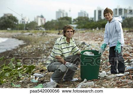 Young male and boy picking up trash on polluted shore View Large Photo Image Stock Photograph - Young male and boy picking up trash on polluted shore. Fotosearch