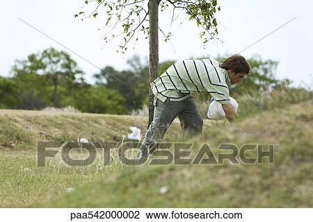 Stock Image - Young male picking up litter in park. Fotosearch