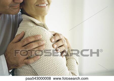 Stock Photo - Man embracing woman from behind, close-up cropped view. Fotosearch