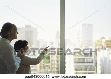 Stock Photography - Mature couple at window looking at view of city skyline, woman pointing. Fotosearch
