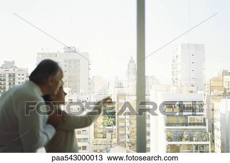 Stock Image - Mature couple looking out view at view of city skyline, woman pointing. Fotosearch