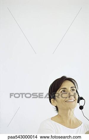 Picture - Mature woman wearing phone headset, smiling, looking up. Fotosearch