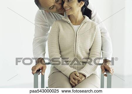 Woman sitting in chair, husband standing behind leaning down whispering in her ear, front view View Large Photo Image Stock Photography - Woman sitting in chair, husband standing behind leaning down whispering in her ear, front view. Fotosearch