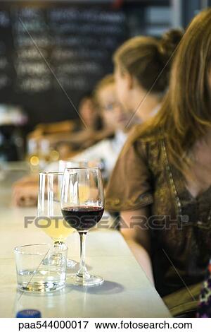 Glasses of wine set on bar, young men and women in conversation in background View Large Photo Image Stock Photo - Glasses of wine set on bar, young men and women in conversation in background. Fotosearch