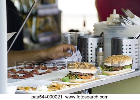 Stock Image - Hamburgers freshly prepared by cook waiting to be served to customers. Fotosearch
