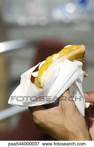 Hand holding hotdog in bun with ketchup and mustard View Large Photo Image Stock Photo - Hand holding hotdog in bun with ketchup and mustard. Fotosearch