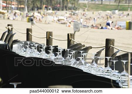 Stock Image - Wine glasses set upside down in rows on table at seaside restaurant. Fotosearch