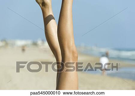Stock Image - Female's legs in air, beach in background. Fotosearch