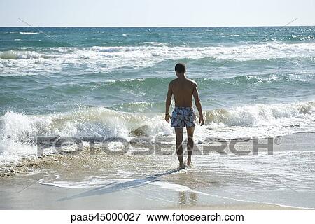Teen boy walking in surf at beach, rear view View Large Photo Image Stock Photo - Teen boy walking in surf at beach, rear view. Fotosearch